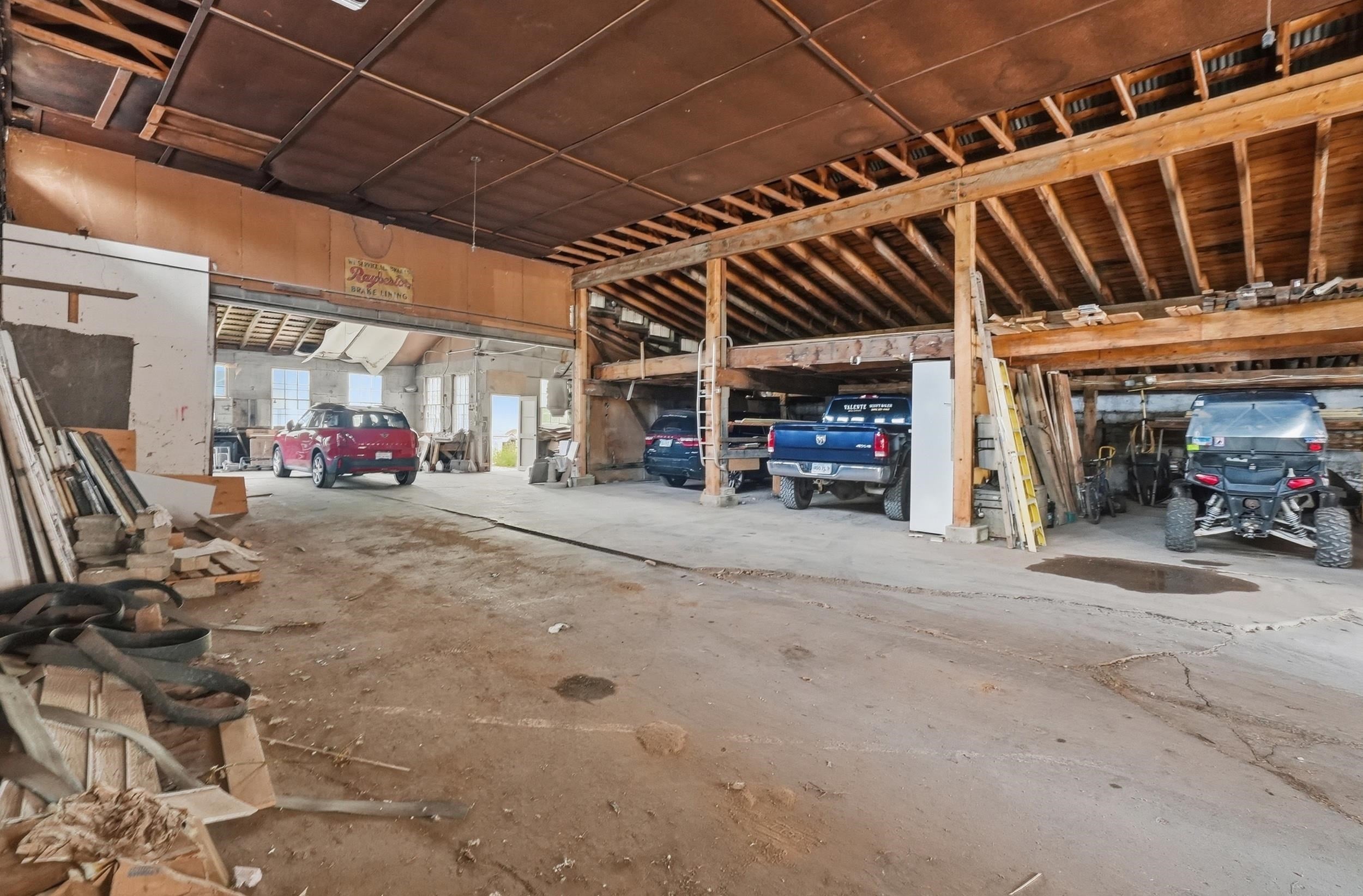 Large workshop garage with exposed rafters, scattered lumber, and several vehicles parked inside.