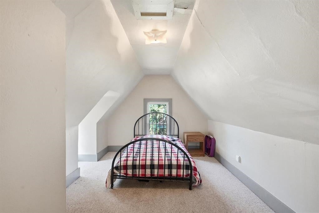 Attic bedroom with sloped ceilings, plaid bedding, and a window at the far end.