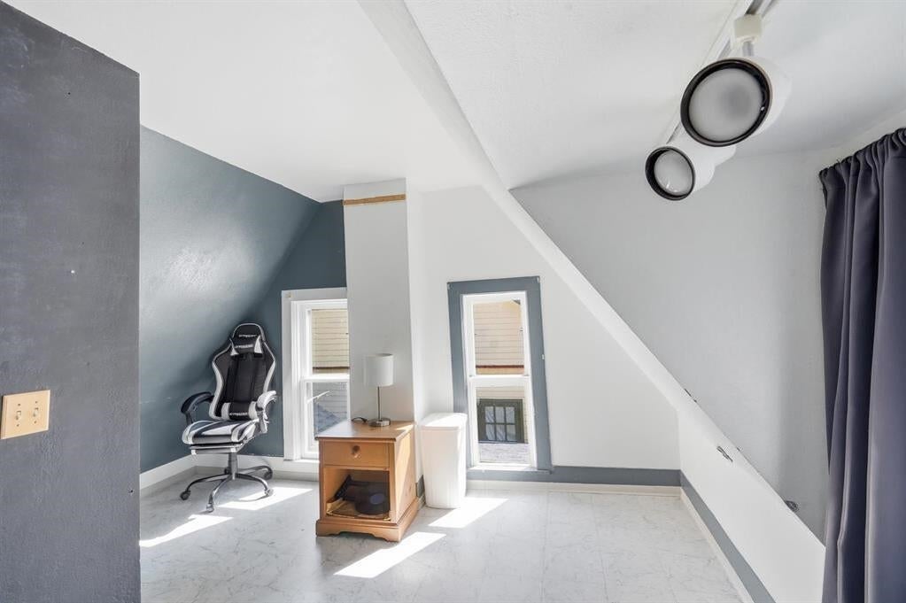 Bright upstairs office with a sloped ceiling, two windows, a small desk, and an office chair.