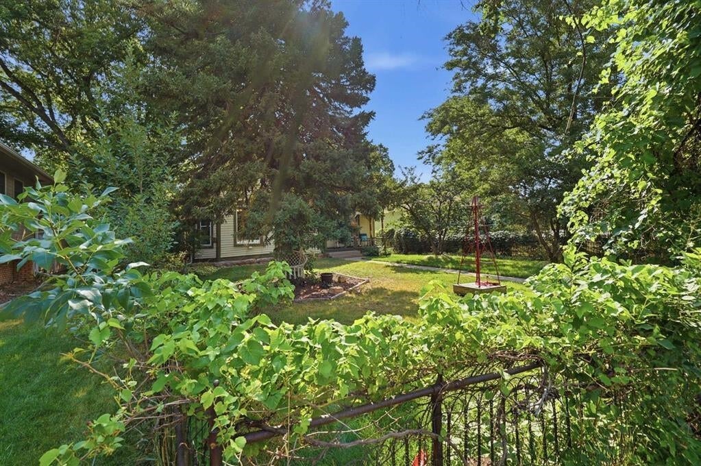 Leafy backyard with a lawn, mature trees, garden beds, and a partly visible house.