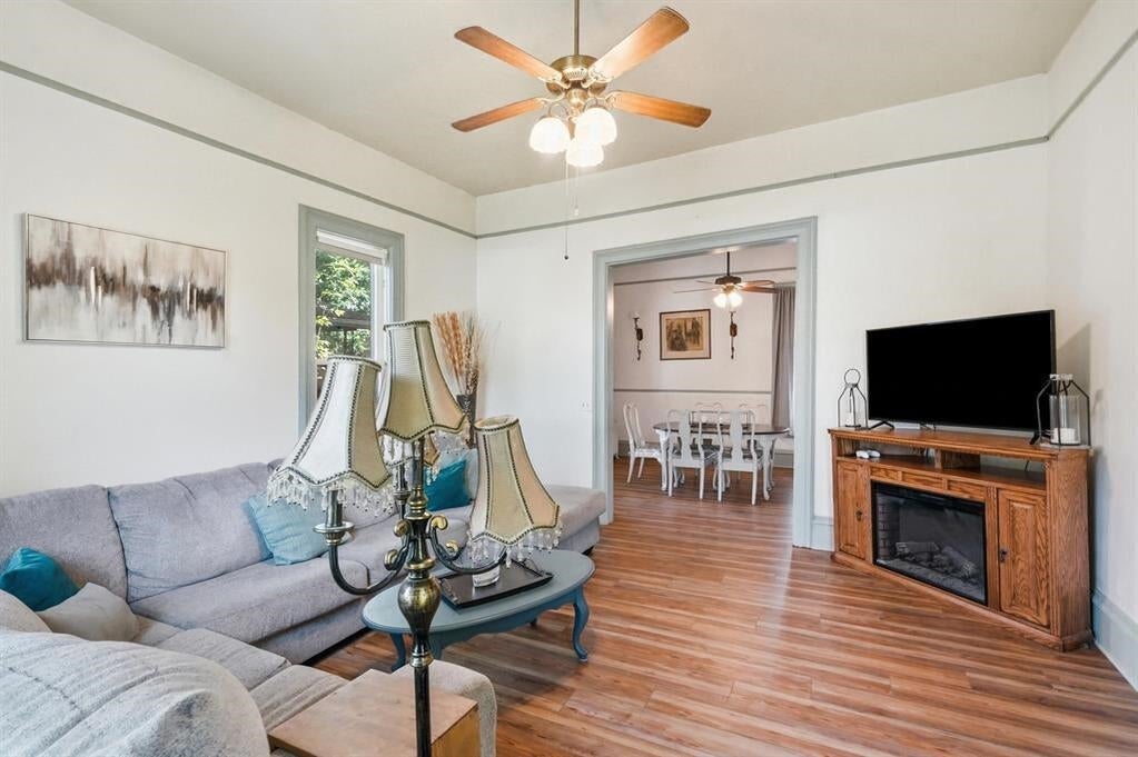Living room with gray sectional sofas, hardwood floors, and a fireplace console beside the dining room doorway.