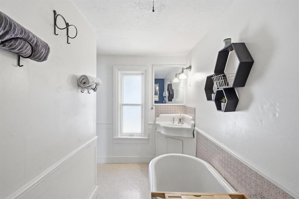Bathroom with a freestanding tub, pedestal sink, tall window, and patterned tile wainscoting.