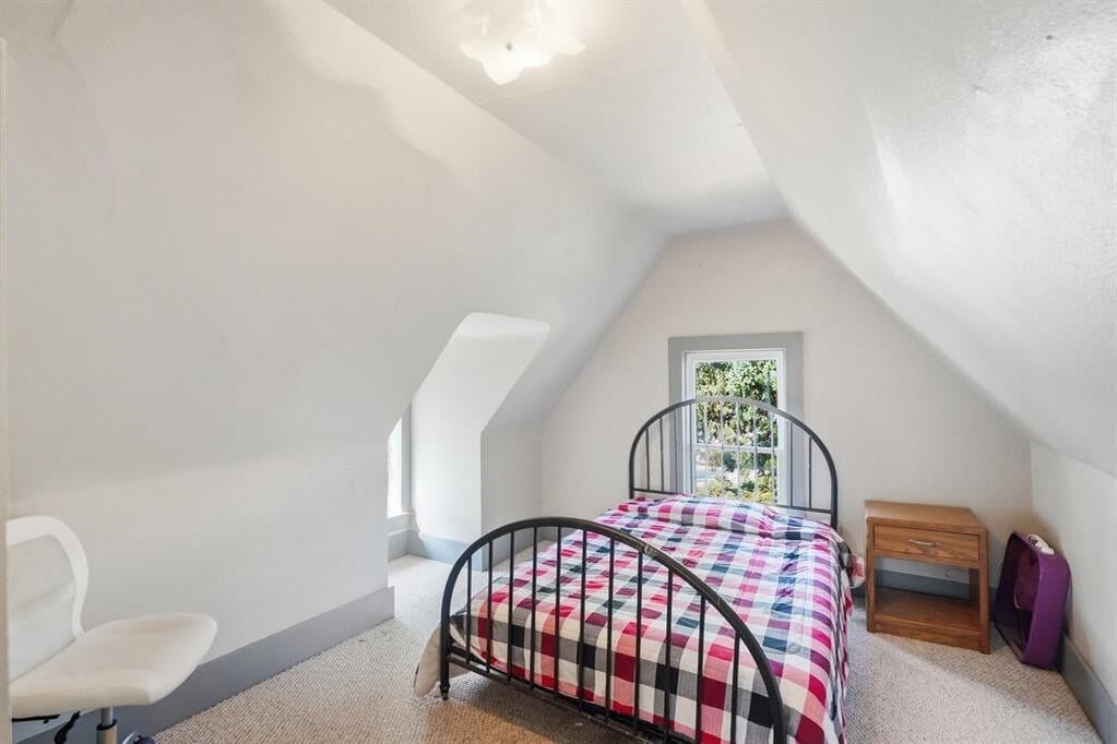 Attic bedroom with a black metal bed, plaid quilt, sloped ceiling, and window behind the bed.