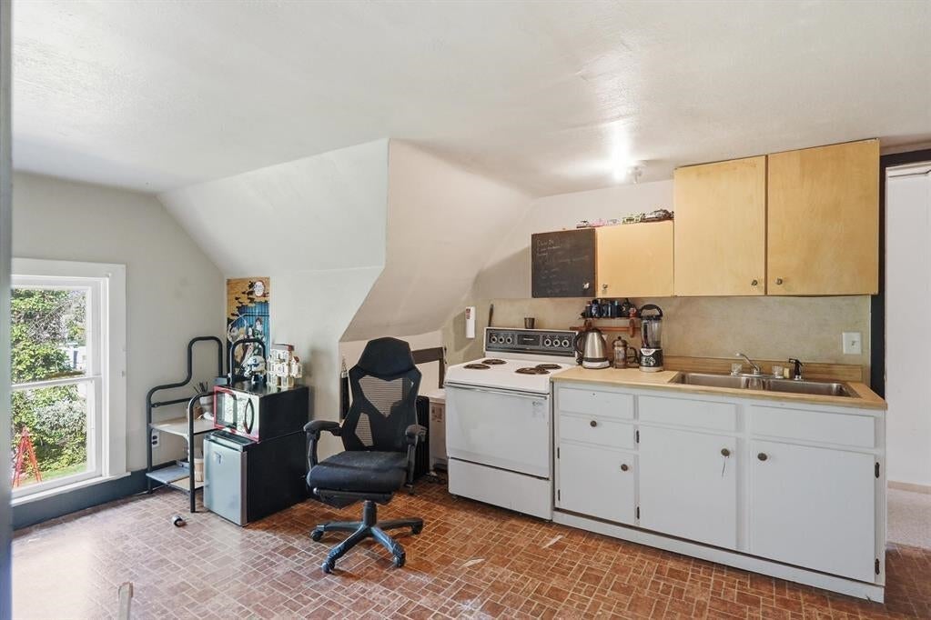 Compact kitchen with white cabinets, electric range, sink, and sloped ceiling.