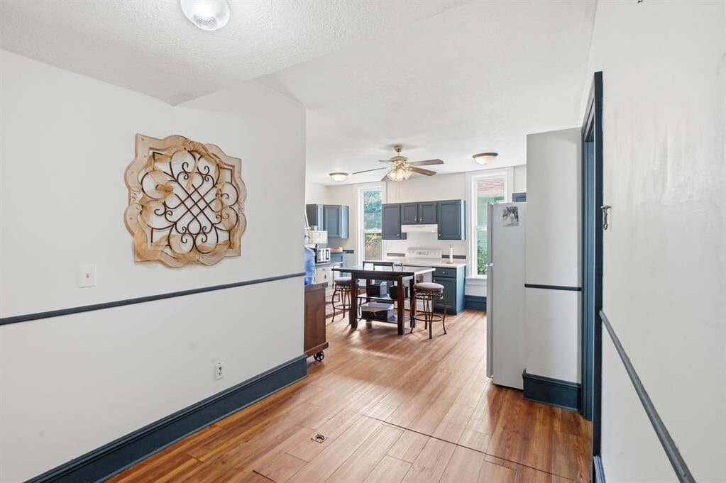 Hallway opening into a blue-cabinet kitchen with a dining table and wood floors.