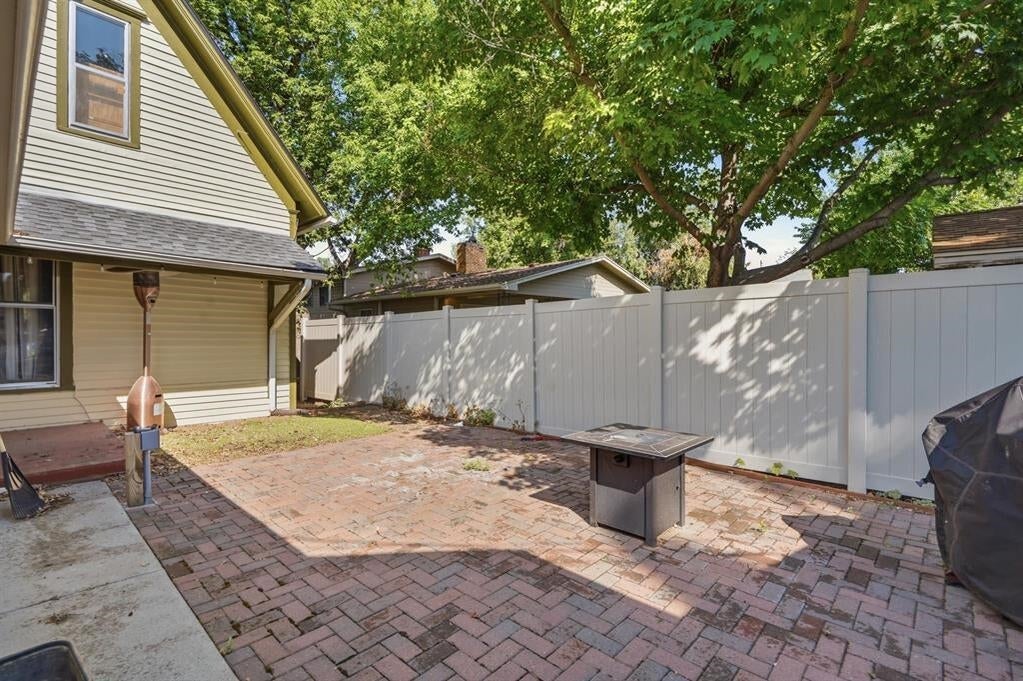 Brick backyard patio with a white privacy fence, shaded by a mature tree.