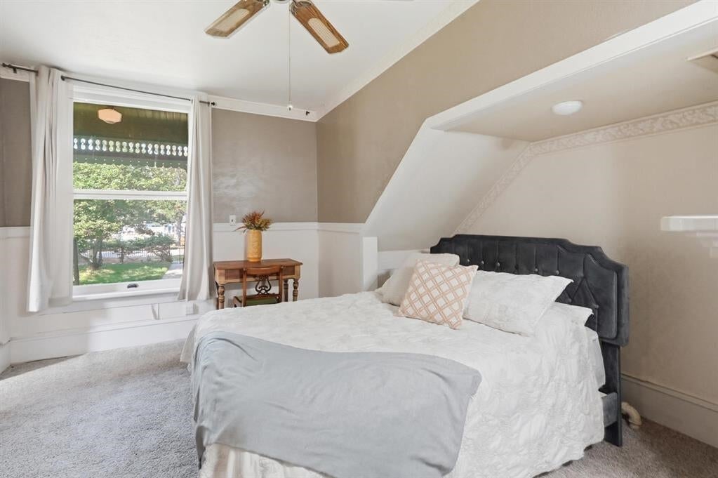 Furnished bedroom with a dark tufted headboard, white bedding, and a window overlooking greenery.