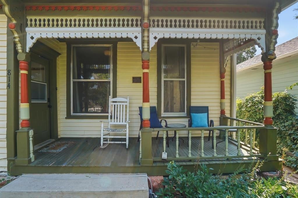 Home’s ornate yellow front porch with Victorian trim, a white rocking chair, and patio seating.
