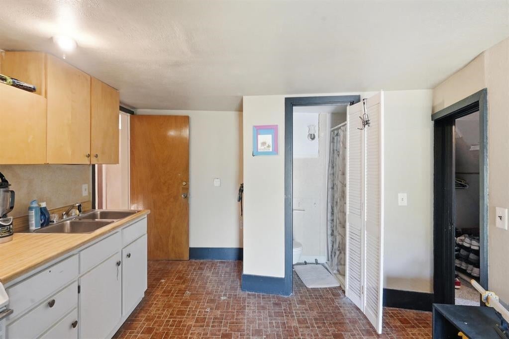 Kitchen with wood cabinets and sink, opening to a bathroom and storage closet.