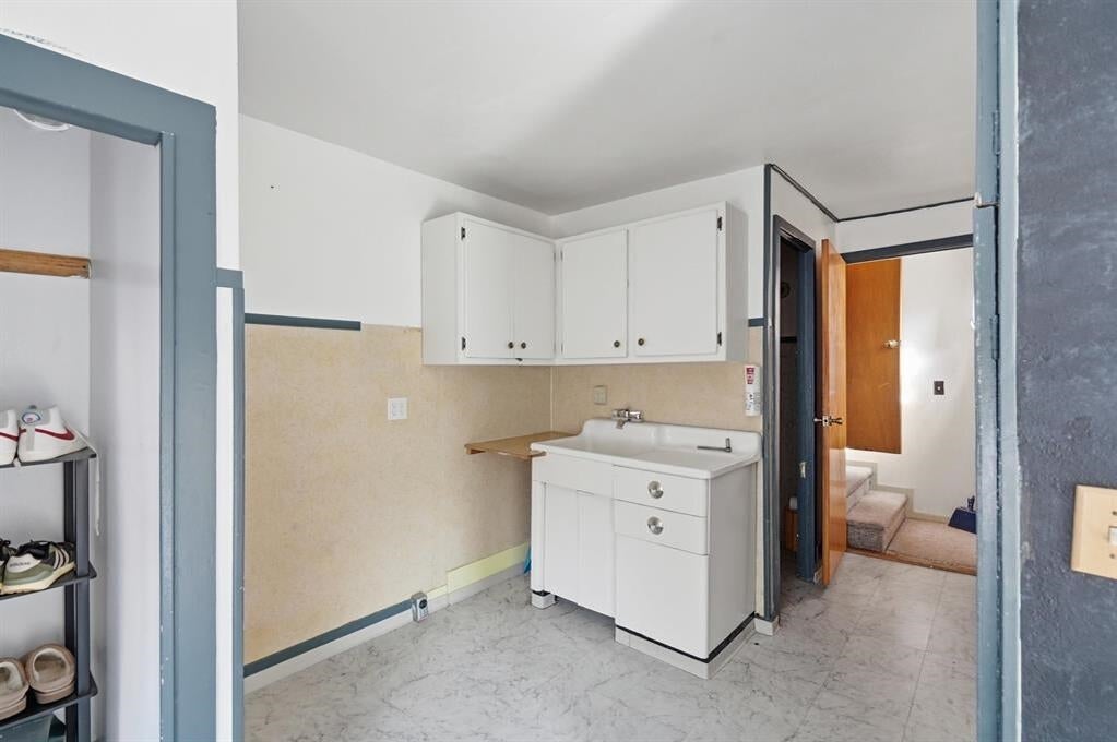 Laundry area with a white utility sink, overhead cabinets, and an open doorway to the hall.