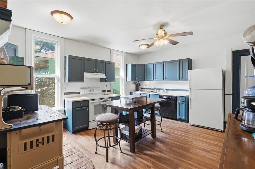 Kitchen with blue-gray cabinets, white appliances, and a wooden island with stools.