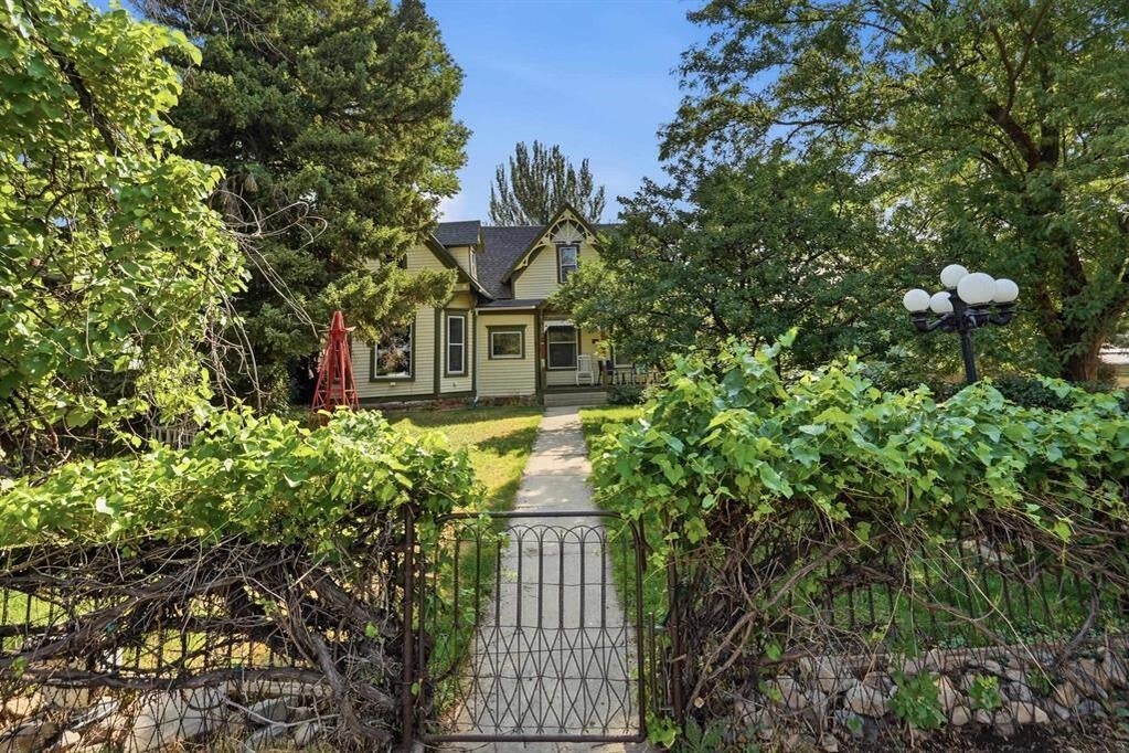 Yellow-sided house beyond a garden gate, with a walkway and mature trees.