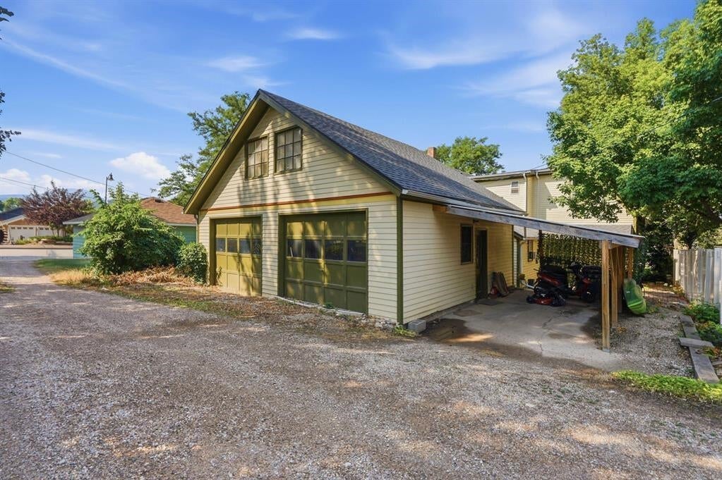 Pale-yellow detached garage with two doors and a covered carport beside a gravel driveway.