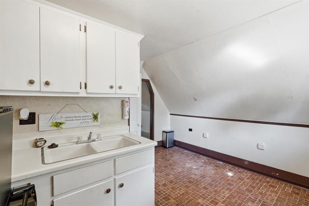 Kitchen with white cabinets and sink beneath a decorative sign, beside a room with a sloped ceiling.