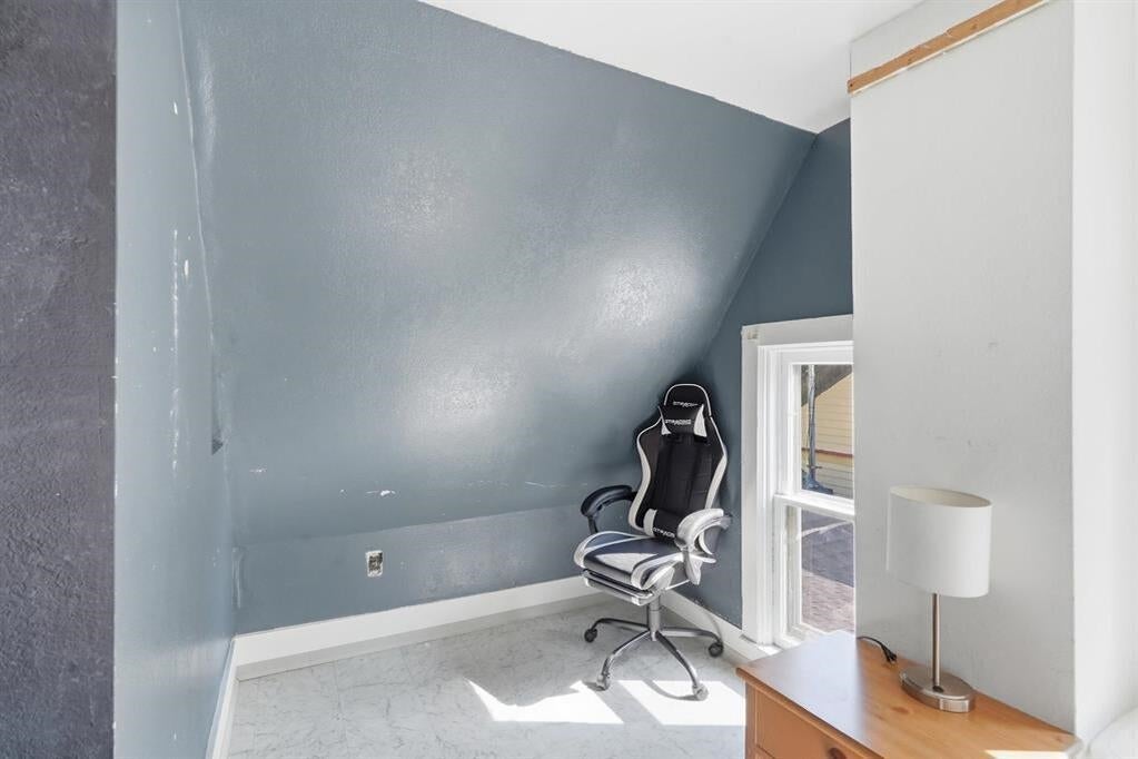 Small blue-gray office with a sloped ceiling, swivel chair, window, and wooden dresser.