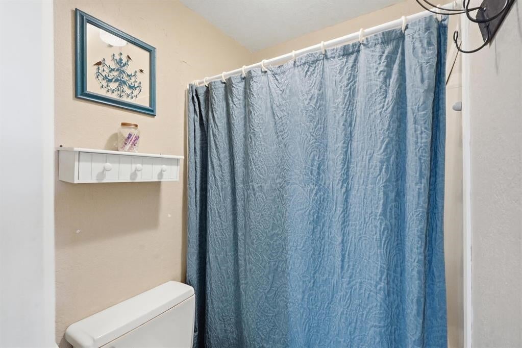 Bathroom with a blue patterned shower curtain, white toilet, and wall shelf.