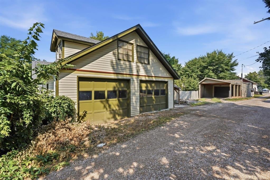Detached garage with two olive-green doors beside a gravel driveway and a smaller garage.