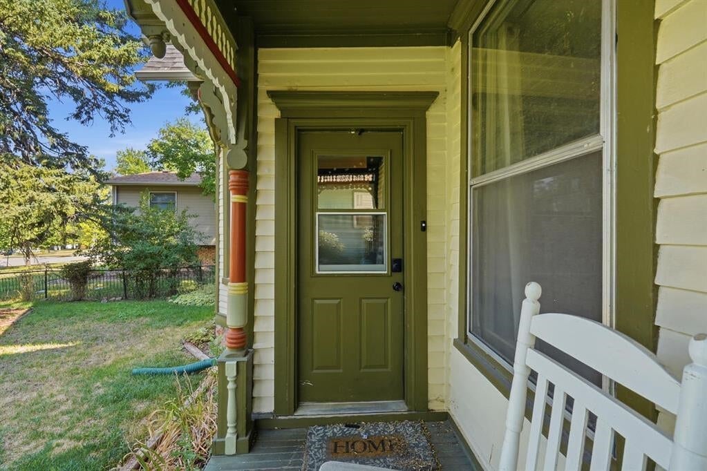 Covered porch with a dark green front door, decorative trim, and a white chair.