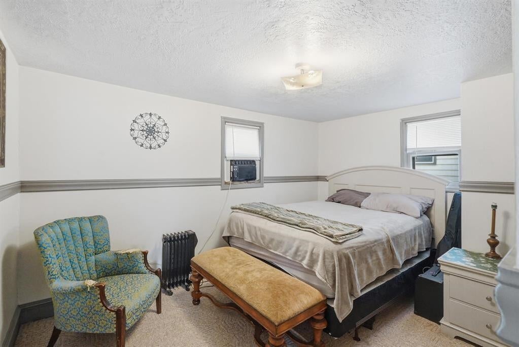 Bedroom with a bed, blue patterned armchair, and window air conditioner.
