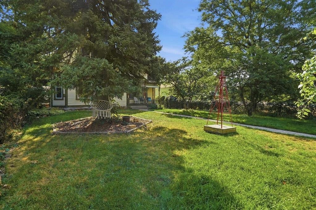 Leafy backyard with a broad lawn, mature trees, garden beds, and a partly obscured house.