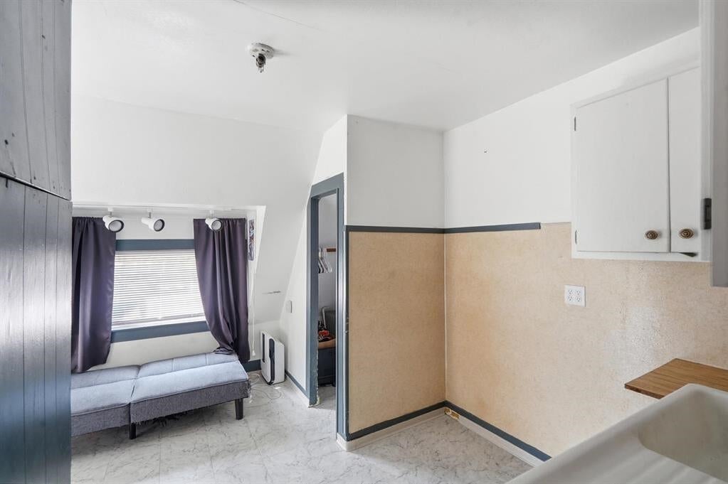 Compact kitchen with a sink and cabinets beside a small sofa nook under a curtained window.