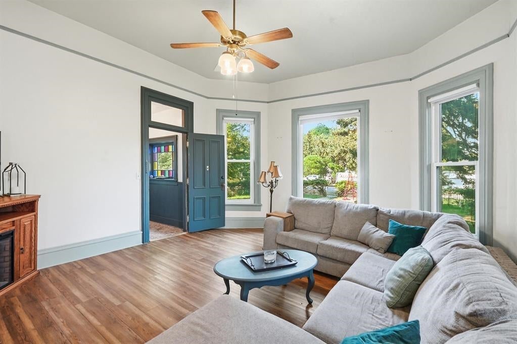 Living room with a gray sectional, blue-trimmed windows, wood floors, and ceiling fan.