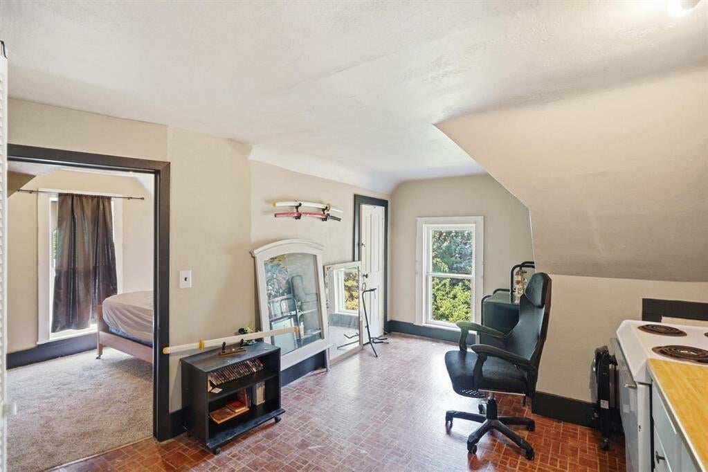 Upper-floor room with a sloped ceiling, patterned floor, stove, and doorway to a bedroom.