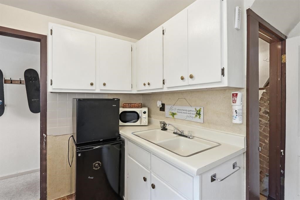Compact kitchen with white cabinets, a sink, black mini fridge, and microwave.