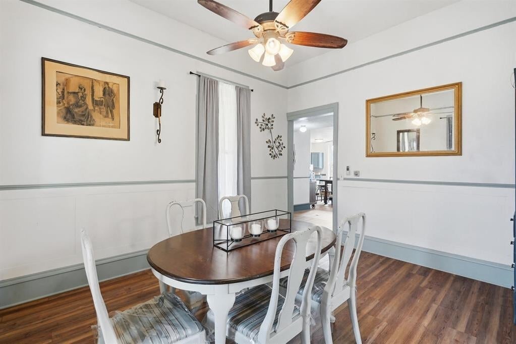Dining room with a round wooden table, white chairs, hardwood floors, and a ceiling fan.