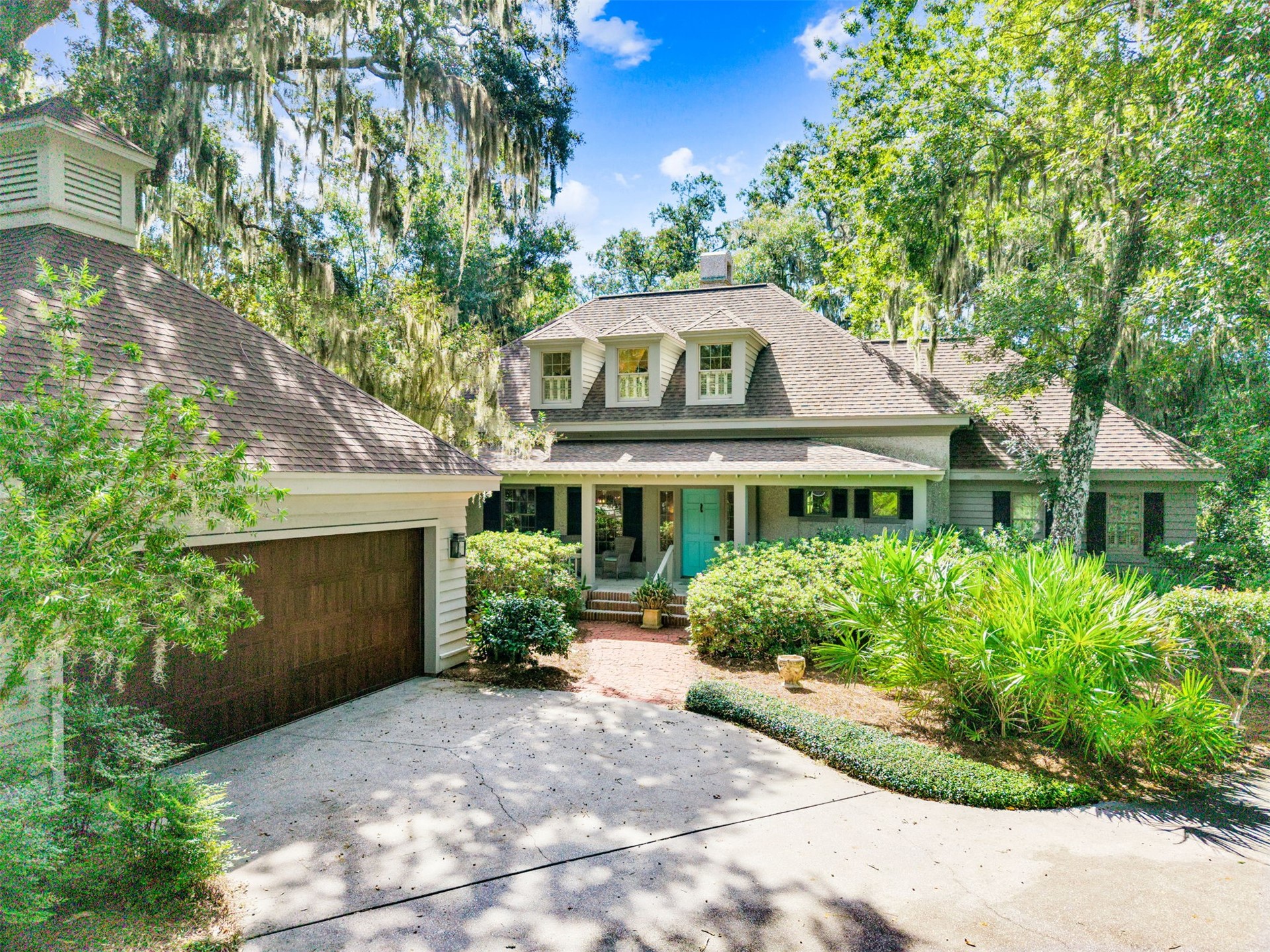 Two-story home with a turquoise front door, attached garage, and mature Spanish moss-draped trees.