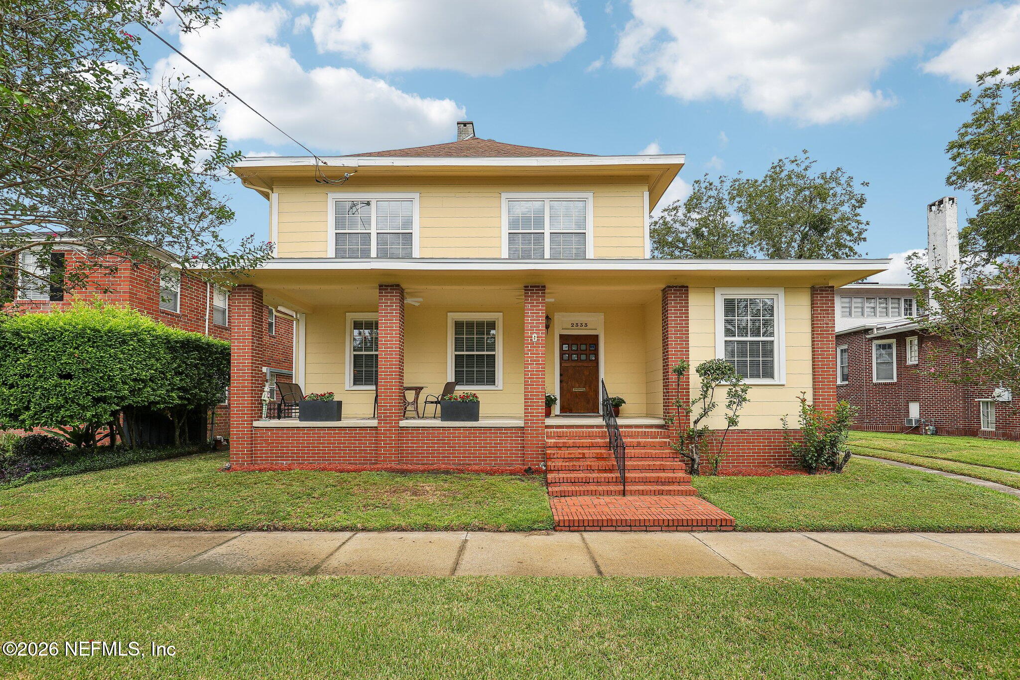 Two-story yellow house with red-brick porch columns, a covered porch, and brick front steps.