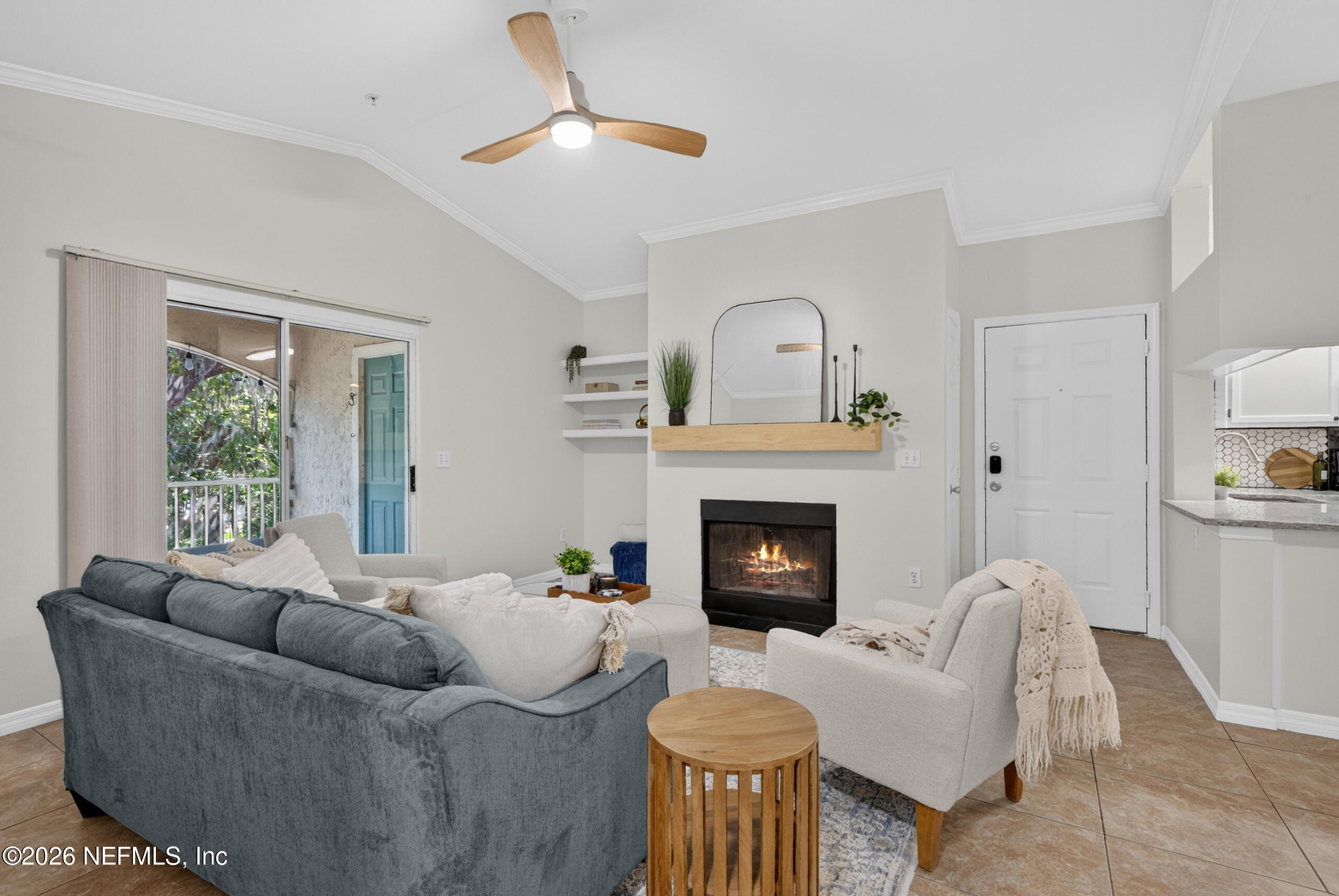 Living room with a fireplace, gray sofa, cream armchairs, and a sliding glass door to a balcony.