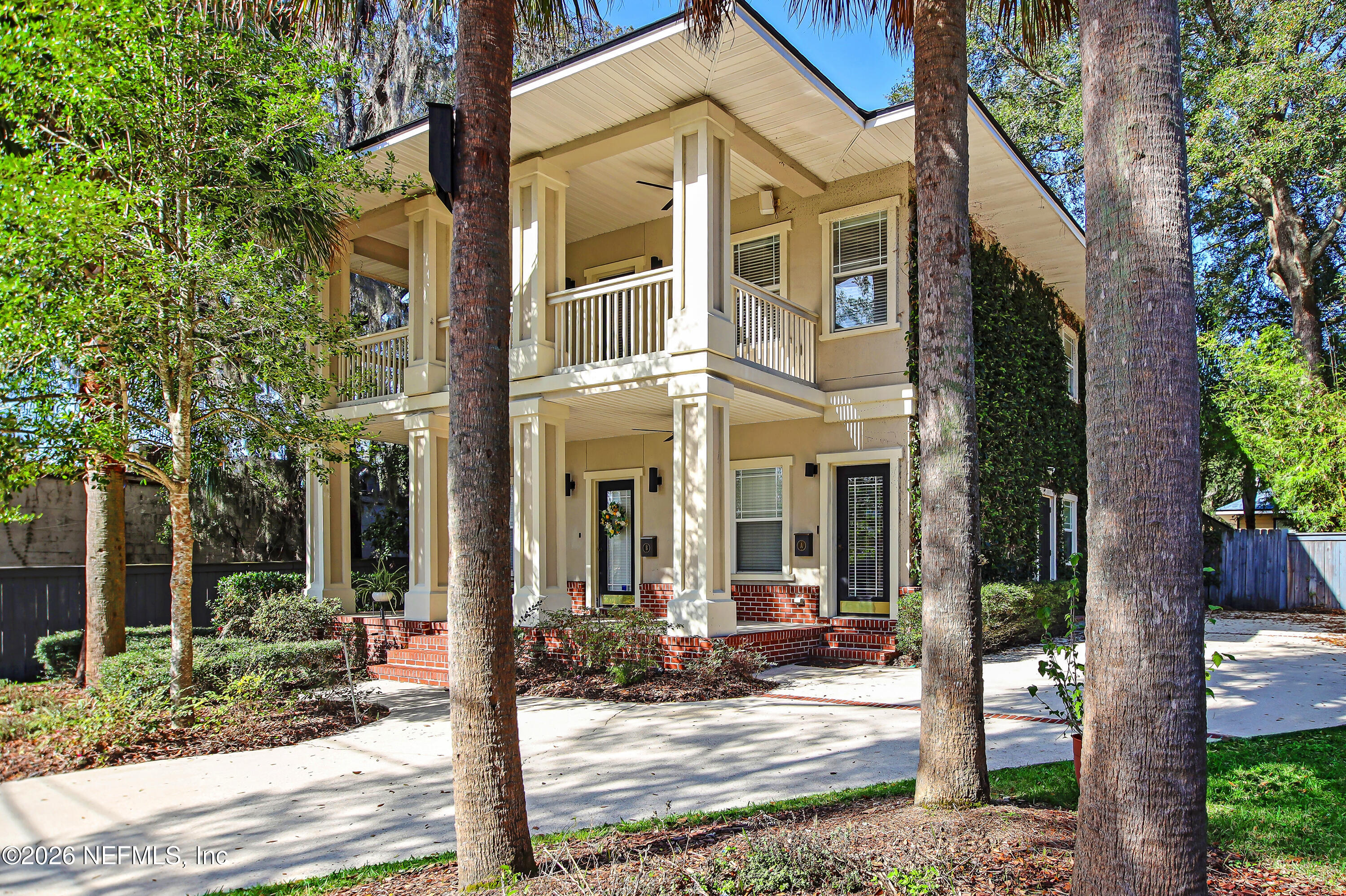 Two-story cream home with columned balconies and red brick steps, framed by palm trees.