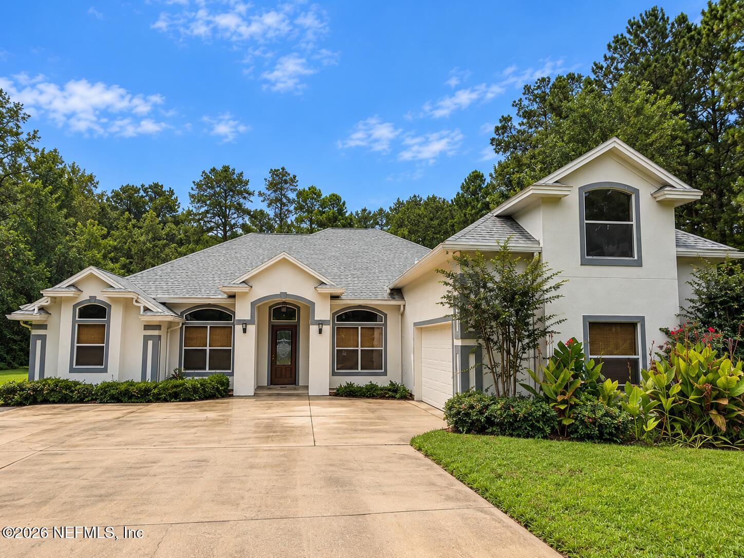 Cream two-story house with gray trim, an attached garage, and a broad driveway framed by mature trees.