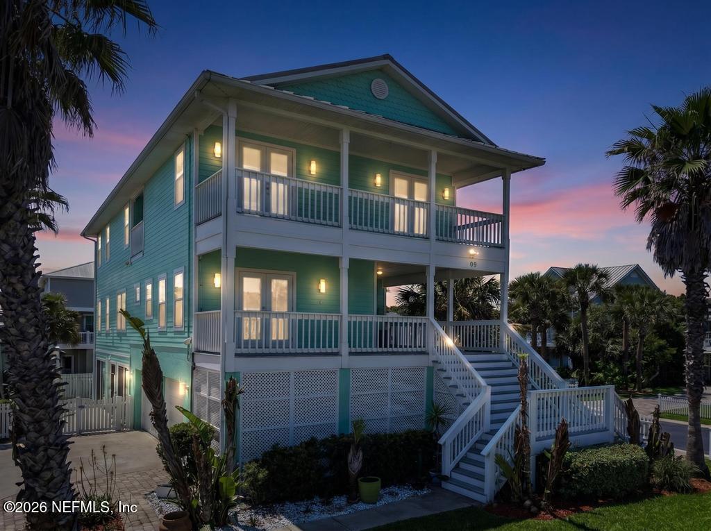Two-story teal house with white-railed porches and an exterior staircase, photographed at dusk.
