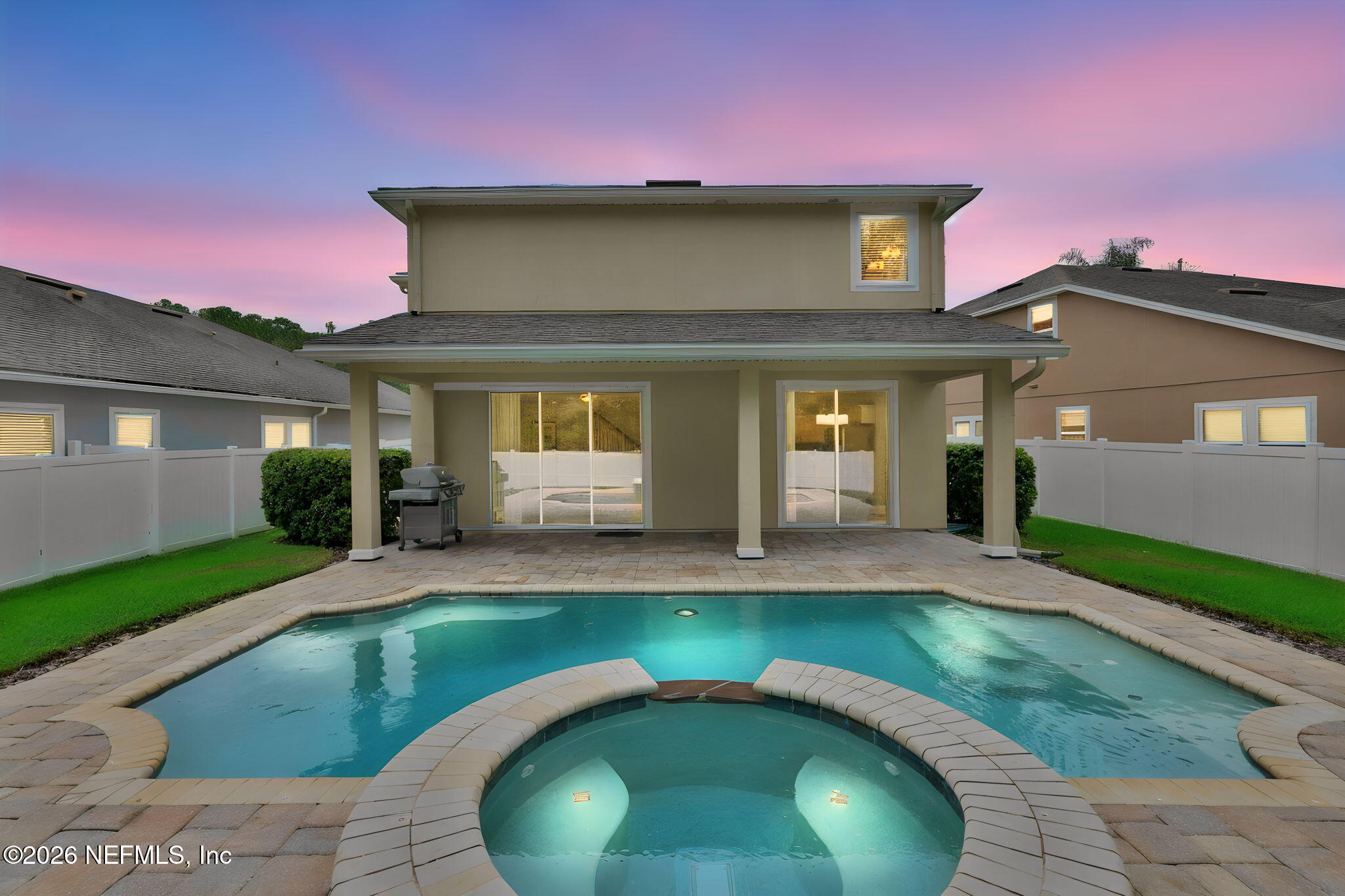 Backyard pool and spa beside a covered patio at dusk.