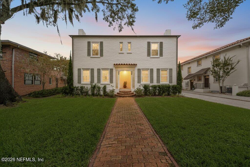 Two-story house at dusk with lit windows and a brick walkway across the lawn.