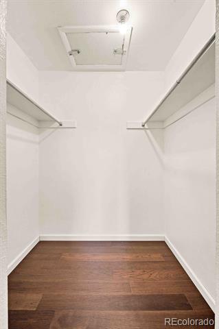 Empty walk-in closet with shelves and hanging rods along both sides and dark wood flooring.