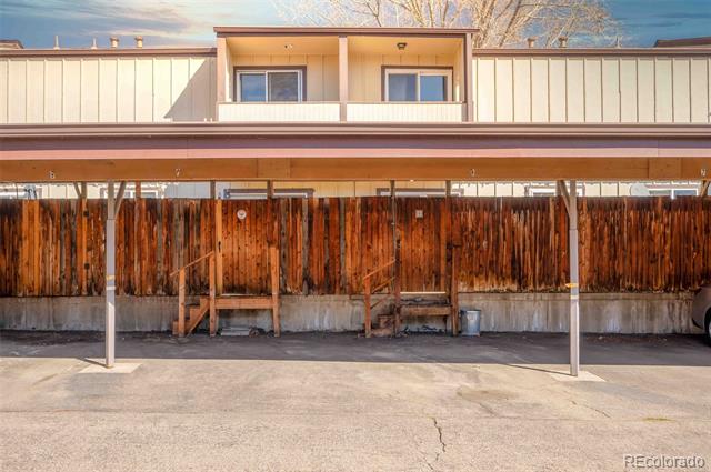 Two-story residential building with upper balconies, covered parking, and a wooden privacy fence.