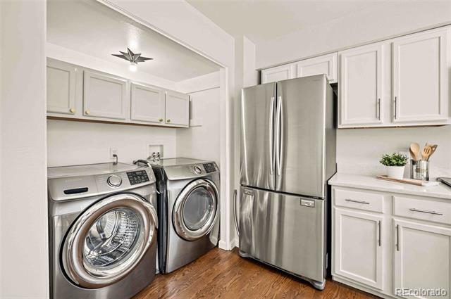 Laundry room with front-loading washer and dryer beside a stainless-steel refrigerator and white cabinetry.