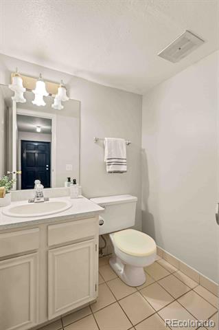 Bathroom with a white paneled vanity, large mirror, toilet, and tan tiled floor.
