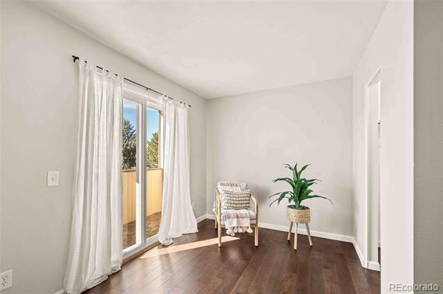 Bright interior room with dark wood floors, a sliding glass door, chair, and potted plant.