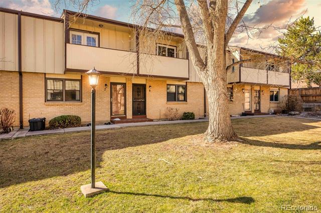 Two-story brick condominium exterior beside a grassy courtyard and large leafless tree.