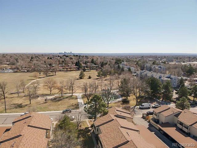 Aerial view of tan-roofed homes beside a leafless park, with a distant city skyline.
