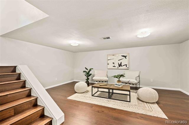 Staged living room with a cream rug and seating beside a wooden staircase.