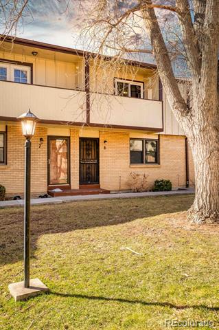 Two-story brick townhouse with a covered balcony, leafless tree, and lawn.