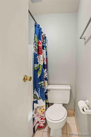 Bathroom with a white toilet, beige tile floor, and blue floral shower curtain.