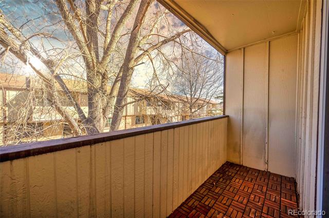 Covered balcony with patterned tile flooring and a view through bare trees toward nearby buildings.