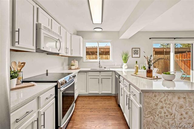 White kitchen with stainless steel appliances, wood flooring, and a peninsula beside a sliding patio door.