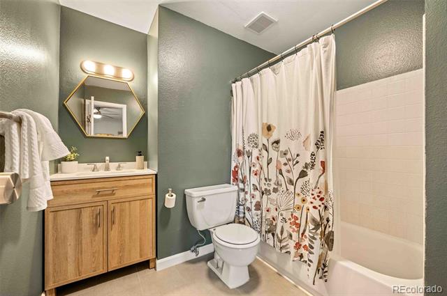 Bathroom with sage-green walls, wood vanity, geometric mirror, and floral shower curtain.